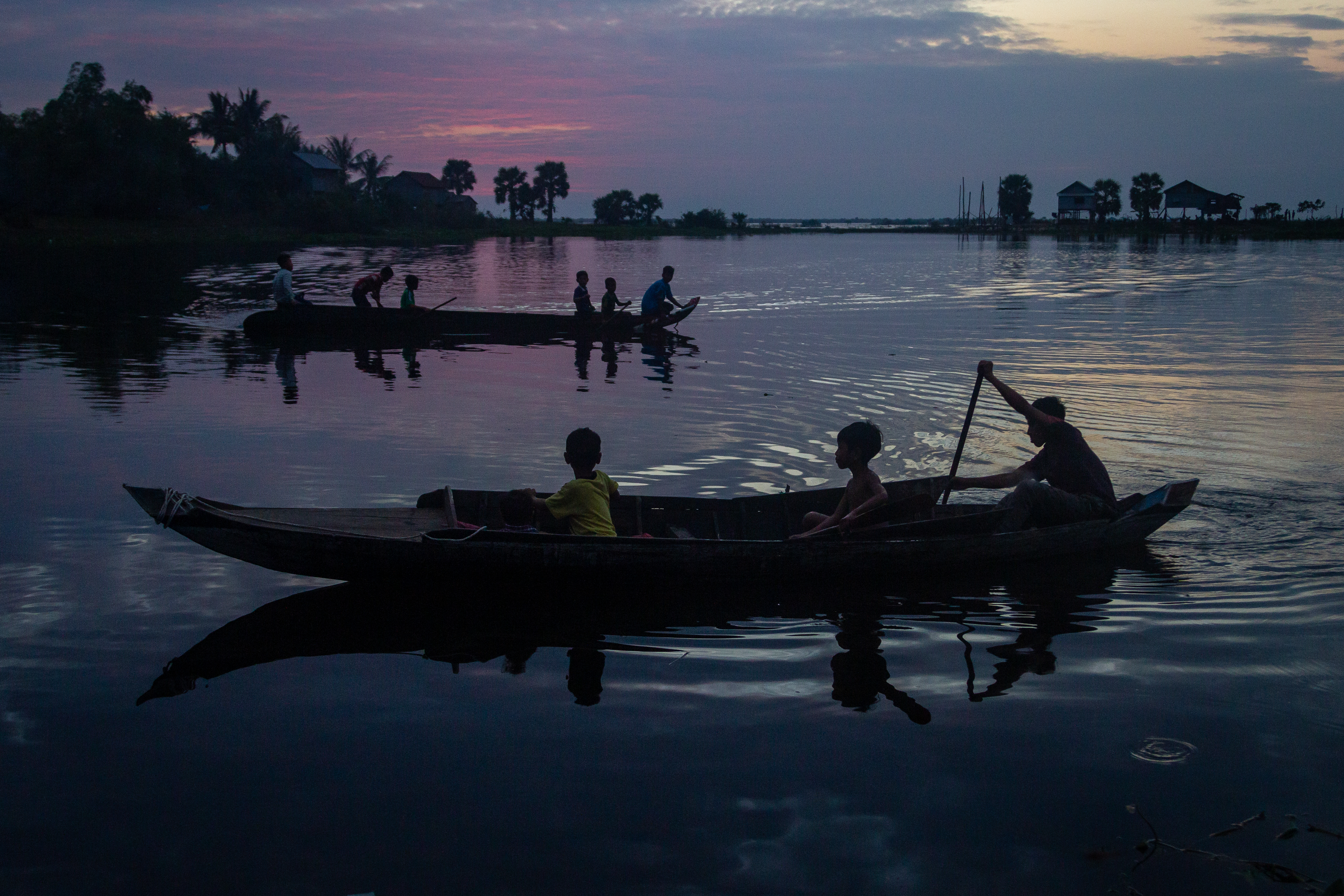 Children row a skiff on on the Tonle Sap lake at dusk in Siem Reap's Phnom Krom village in December 2017. 