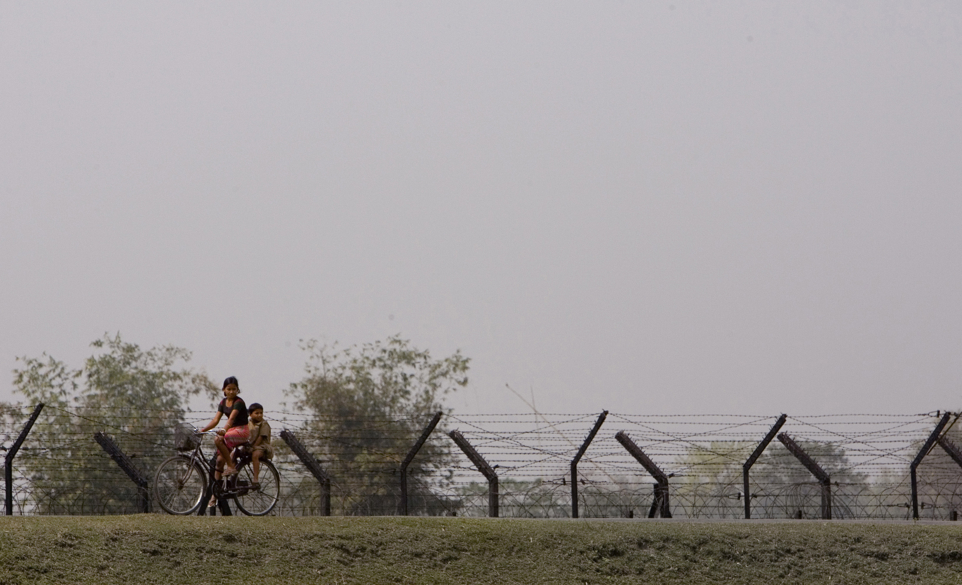 Children bike past a fence separating India from Bangladesh in February 2007. The two countries share a 2,545-mile long border, some three-quarters of which has been fenced off in recent years as the Indian government looks to crack down on migration. 