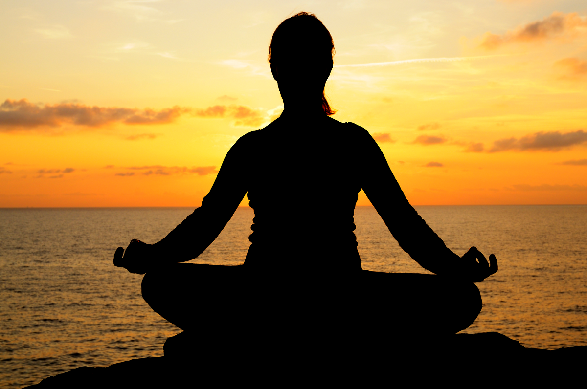 A woman meditating facing the sunset