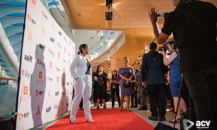 Full body photograph of a woman in a white suit in profile, standing on a red carpet inside Asia Society New York