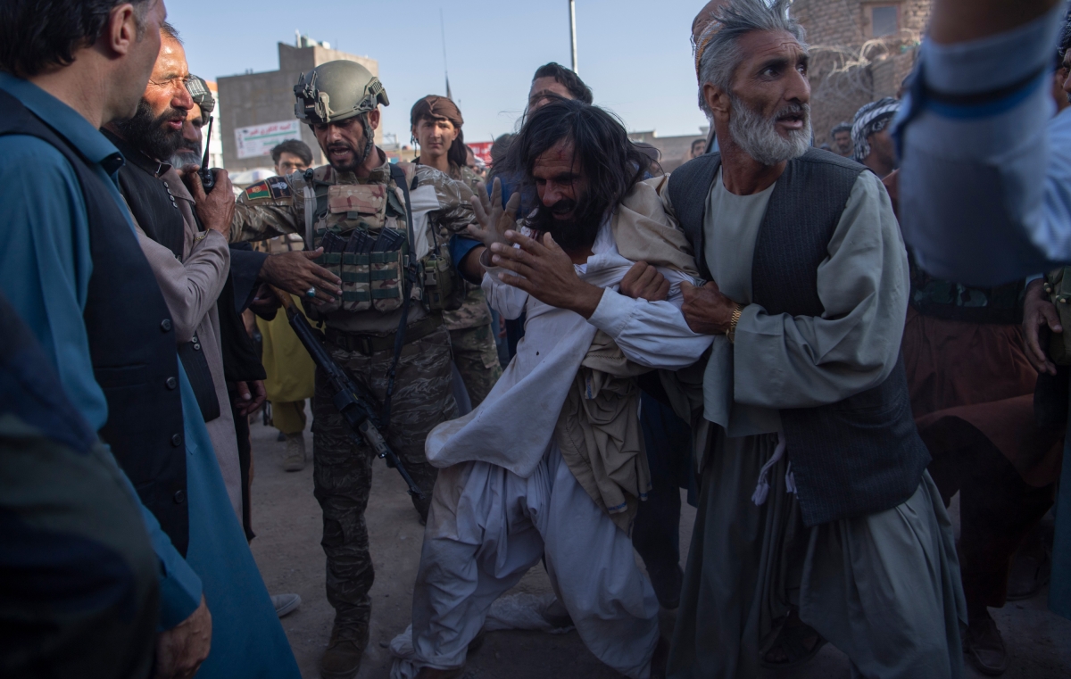 A member of the Afghan military tries to intervene as a militia member detains and beats a suspected Taliban insurgent in Herat on August 2, 2021. Militias emerged to fight the Taliban in places where Afghan security forces were insufficient. Security forces who were there reported being powerless to prevent the militia members from violently attacking the Taliban.