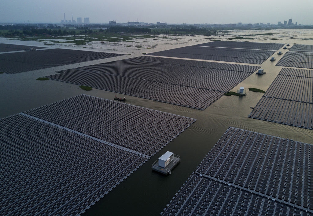Chinese workers ride in a boat through a large floating solar farm project under construction by the Sungrow Power Supply Company on a lake caused by a collapsed and flooded coal mine on June 13, 2017 in Huainan, Anhui province, China. The floating solar field is billed as the largest in the world. (Kevin Frayer/Getty Images)
