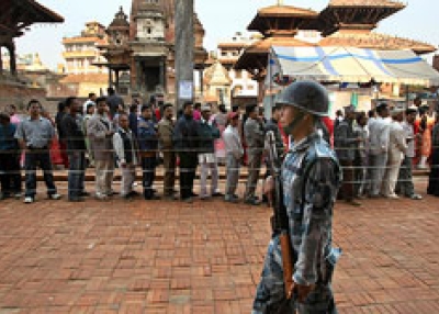 Kathmandu, April, 10, 2008 - As the country goes to the polls, Nepalese men queue to cast their ballots while a soldier patrols the streets. (PEDRO UGARTE/AFP/Getty Images)