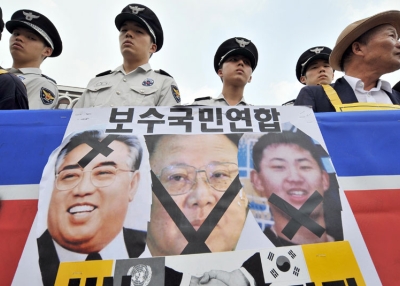 South Korean police watch a conservative activists standing behind a North Korean flag with pictures of the North's late president Kim Il-Sung (L), his son and current leader Kim Jong-Il (C) and grandson Kim Jong-Un (R), during an anti-Pyongyang rally in Seoul on July 8, 2009. (Jung Yeon-Je/AFP/Getty Images)