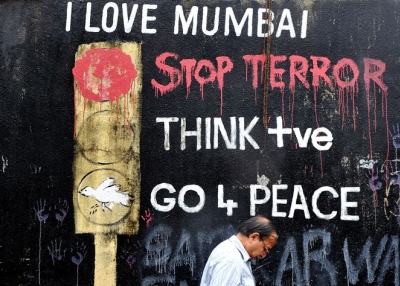 An Indian office worker walks past wall graffiti made after the 2008 terror attacks near the recent blast site at Opera House in Mumbai on July 14, 2011. (Indranil Mukherjee/AFP/Getty Images)