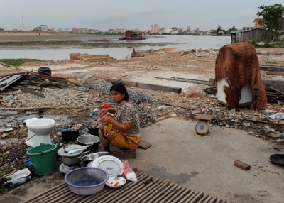 A Cambodian woman washing dishes outside her house on the edge of the Boeung Kak lake (background) in central Phnom Penh as debris from destroyed buildings litter the ground nearby on May 25, 2011. (Christophe Archambault/AFP/Getty Images)