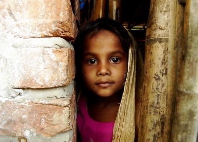 A little girl looks at the camera from behind a brick wall in Teknaf, Bangladesh on November 13, 2012. (No_Direction_Home/Flickr)