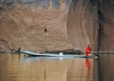 Dressed in bright red, a boatman paddles his way through calm waters in Laos on March 19, 2014. (jean jacques chaffois/Flickr)