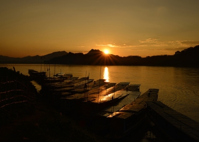 Streaks of the setting sun illuminate a row of boats moored by the Mekong River near Laos on November 17, 2014. (Tartarin2009/Flickr)