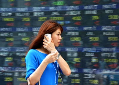 A woman passes before a share prices board in Tokyo