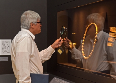A museum visitor uses a magnifying glass to inspect an item curated in the 'Philippine Gold' exhibition.