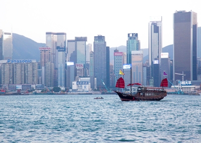 A junk boat with dark, red sails glides past the tall buildings of Hong Kong Island on November 28, 2015. (Tahiat Mahboob)