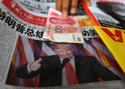 A vendor picks up a 100 yuan note above a newspaper featuring a photo of U.S. president-elect Donald Trump, at a news stand in Beijing on November 10, 2016. (Greg Baker/AFP/Getty Images)