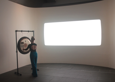 Person playing a large gong in front of a light artwork.