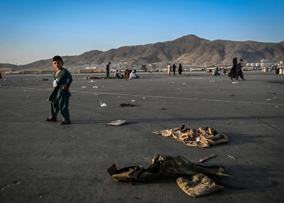 An Afghan child walks near military uniforms as he with elders wait to leave the Kabul airport, after a stunningly swift end to Afghanistan's 20-year war, as thousands of people mobbed the city's airport trying to flee