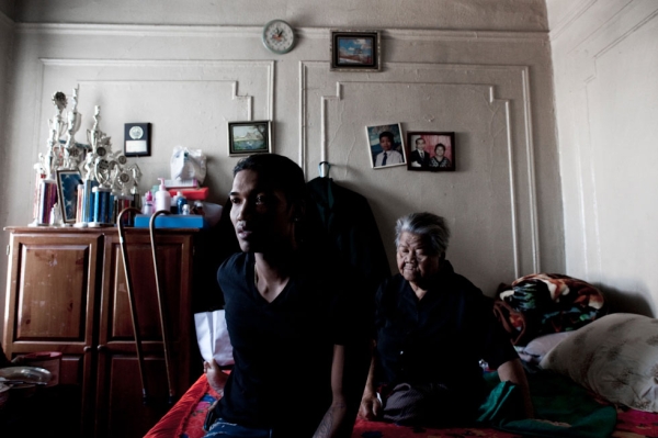 Sovann Ith, 23, sits alongside his grandmother, Somaly Ith, 83, in the living room of their Bronx apartment. (Pete Pin)