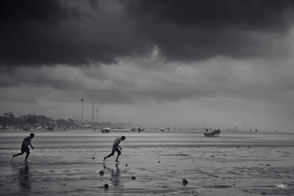 As storm clouds gather, two boys run on the Marina Beach in Chennai, India on November 2, 2012. (VinothChandar/Flickr)