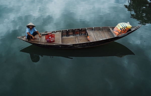 A boat and its occupant reflected in calm blue waters in Hoi An, Vietnam on June 11, 2014. (ilya/Flickr)