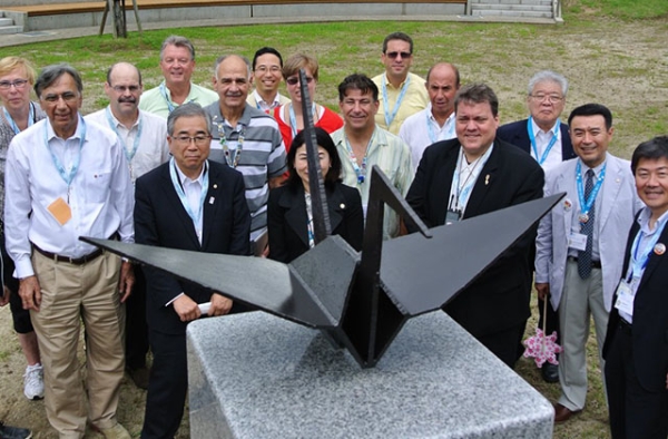 Participants in an exchange between 9/11 and 3/11 survivors pose in Kaisezan Park, Koriyama, Fukushima Prefecture with a steel origami crane in 2013. The crane was fashioned from World Trade Center wreckage and presented by the 9/11 Tribute Center on the first outreach trip in 2012. (9/11 Tribute Center)
