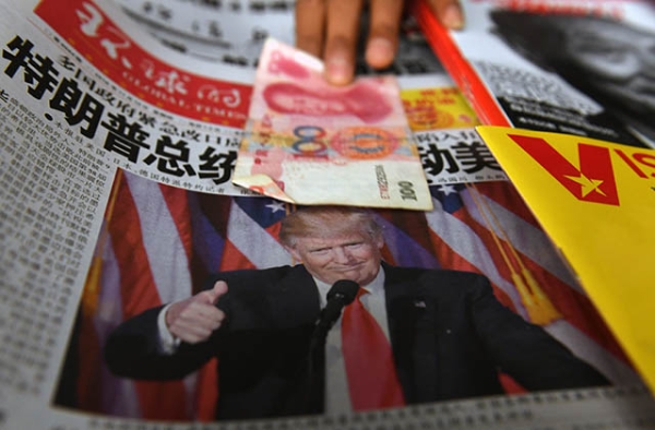 A vendor picks up a 100 yuan note above a newspaper featuring a photo of U.S. president-elect Donald Trump, at a news stand in Beijing on November 10, 2016. (Greg Baker/AFP/Getty Images)