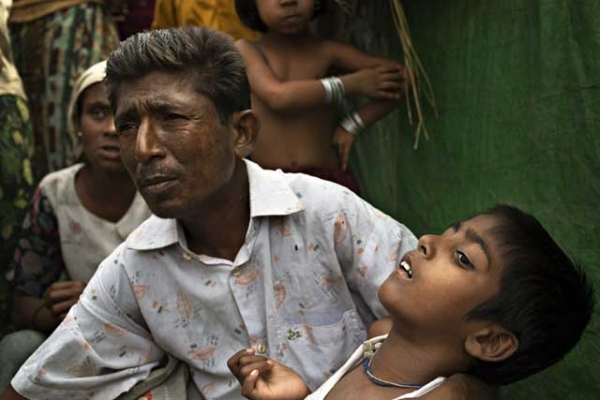 Roshida Moud, 12, is held by his father as the latter explains that his son was hit in the head with a stone during the Rakhine violence in 2012, in Sittwe, Myanmar, on May 6, 2014. (Andre Malerba/Getty Images)