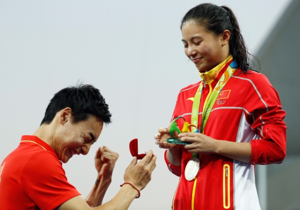 Chinese diver Qin Kai proposes to silver medalist He Zi of China on the podium during the medal ceremony for the Women's Diving 3m Springboard Final. (Clive Rose/Getty Images)