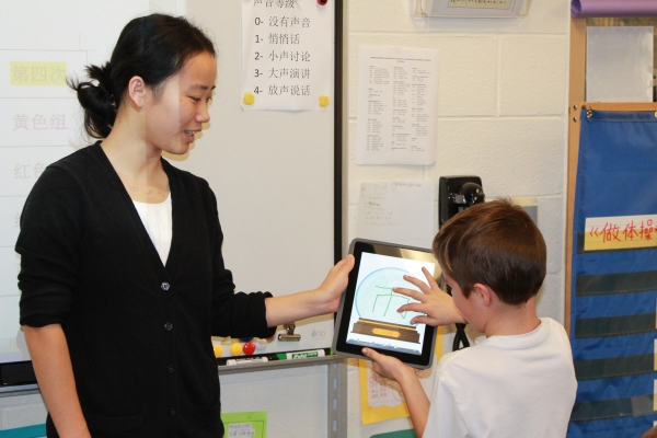 A student works with his teacher to write the appropriate Chinese character on an electronic tablet.