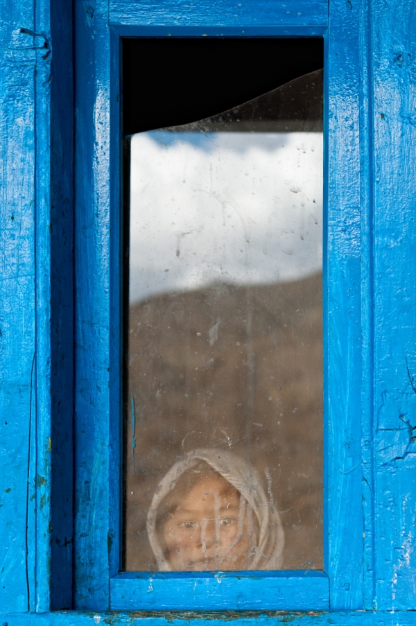 A girl peers out a brilliant blue window in Khangral. (Anjum Vahanvati)