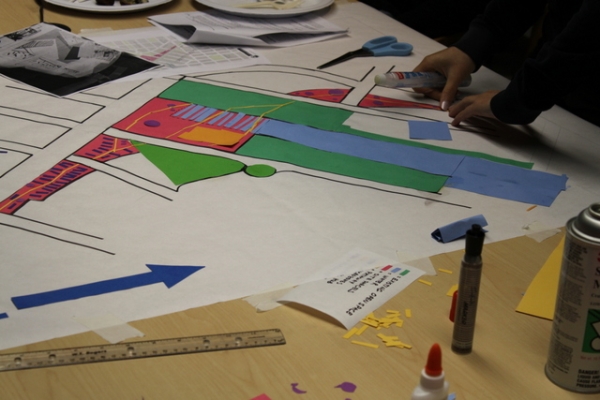 Team members work on a large cut-paper conceptual layout of the site redesign