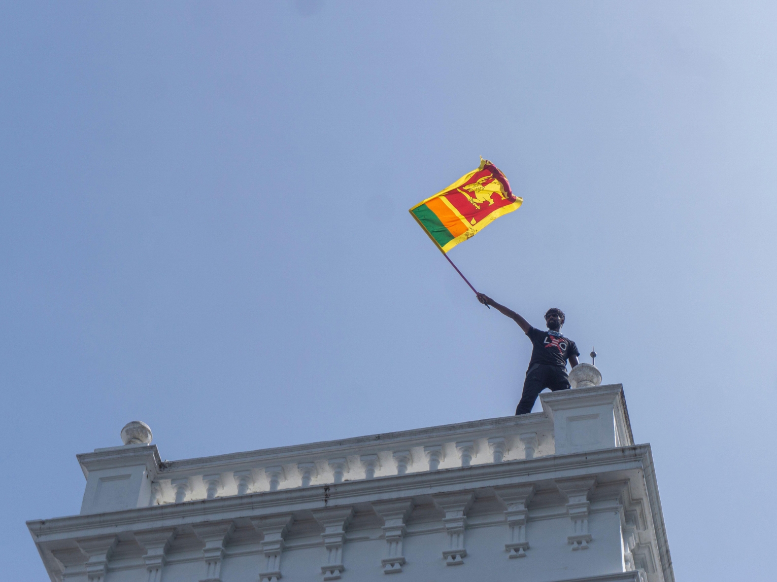 A protester waves a Sri Lankan flag while standing atop prime minister Ranil Wickremesinghe's office in Colombo on July 13, 2022. Hundreds of protesters stormed the office amid the deep political and economic crisis in the country which led to months of widespread protests.