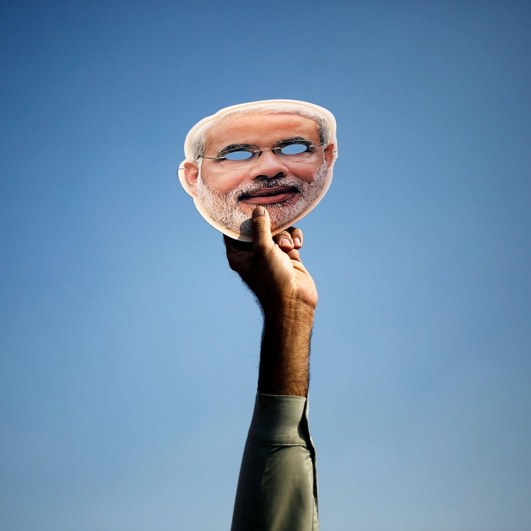 A raised hand holds a mask depicting Indian Prime Minister Narendra Modi.