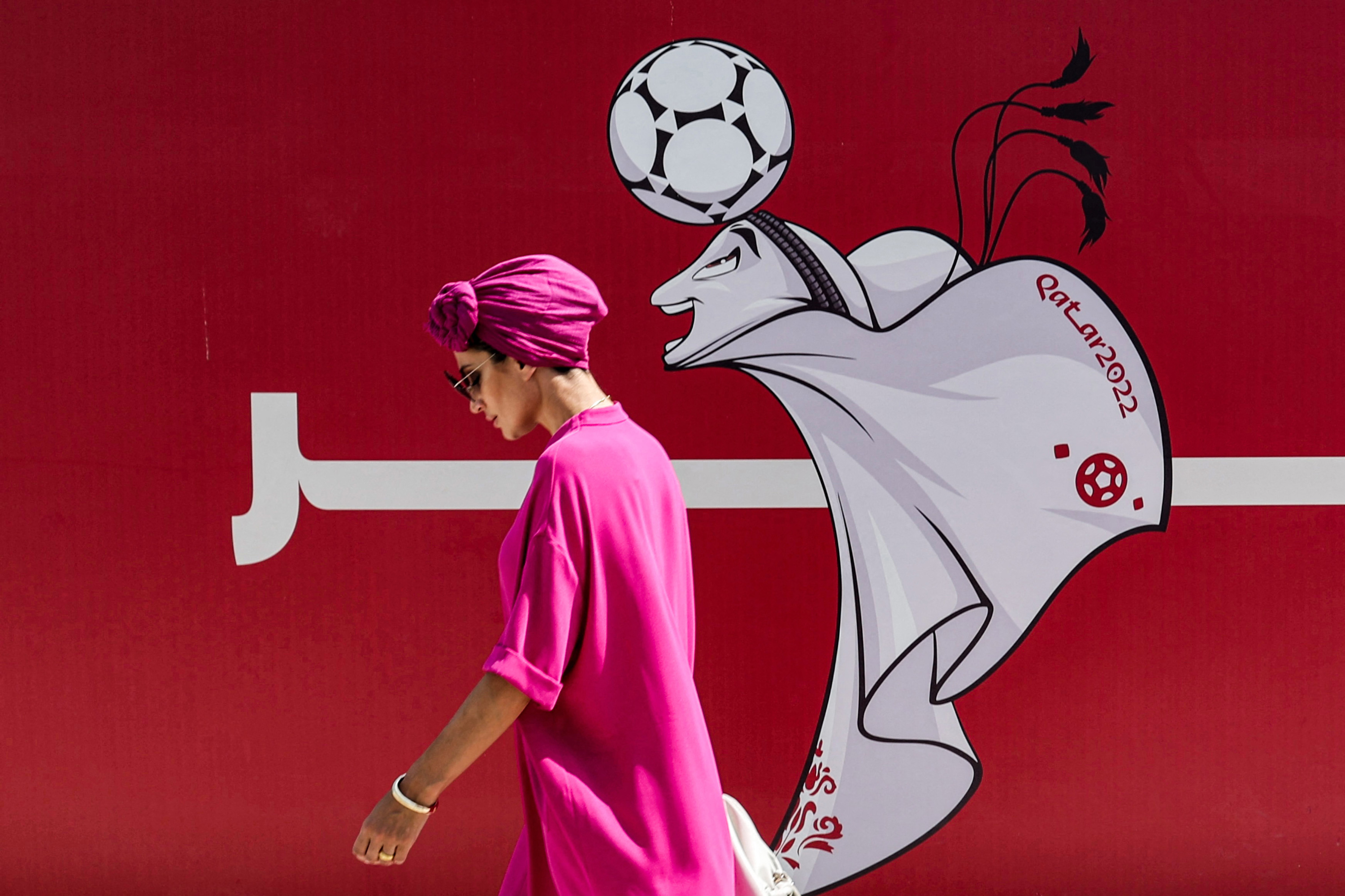 A woman walks past a construction site fence showing an illustration of the Qatar 2022 FIFA World Cup mascot "La'eeb" in West Bay in Qatar's capital Doha on October 13, 2022.