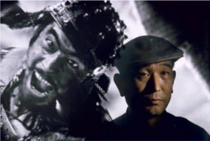 Brian Brake: Film director Akira Kurosawa standing before an image of his principal star, Toshiro Mifune, Tokyo, Japan, 1963