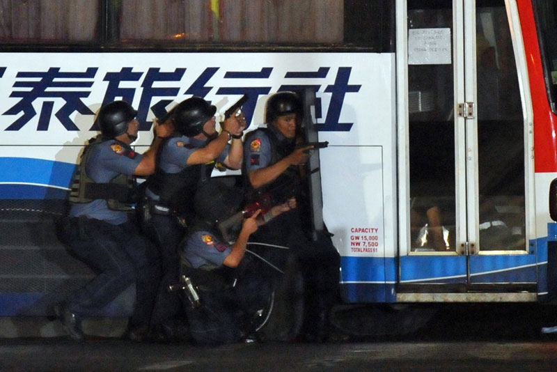 Philippine policemen take cover as they start their assault on the tourist bus full of Hong Kong tourists after an ex-policeman hijacked the bus in Manila on August 23, 2010. (Ted Aljibe/AFP/Getty Images)