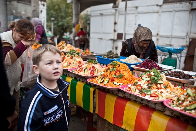 A young ethnic Russian boy stands in front of a wide array of cold salads in the Jalalabad Bazaar. (Sue Anne Tay)