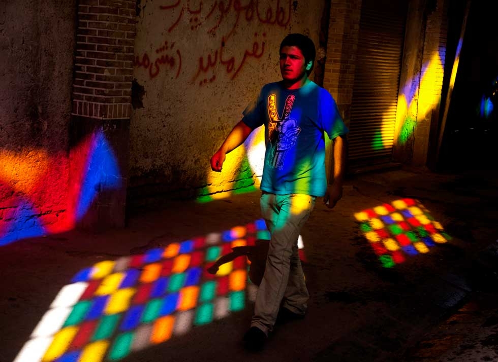  A young Iranian man walks through light from a stained glass window in Tehran Bazaar. (Amos Chapple)