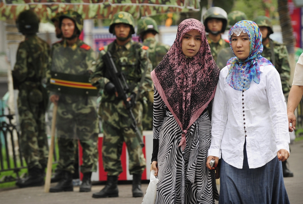 Two ethnic Uighur women pass Chinese paramilitary policemen standing guard outside the Grand Bazaar in the Uighur district of the city of Urumqi