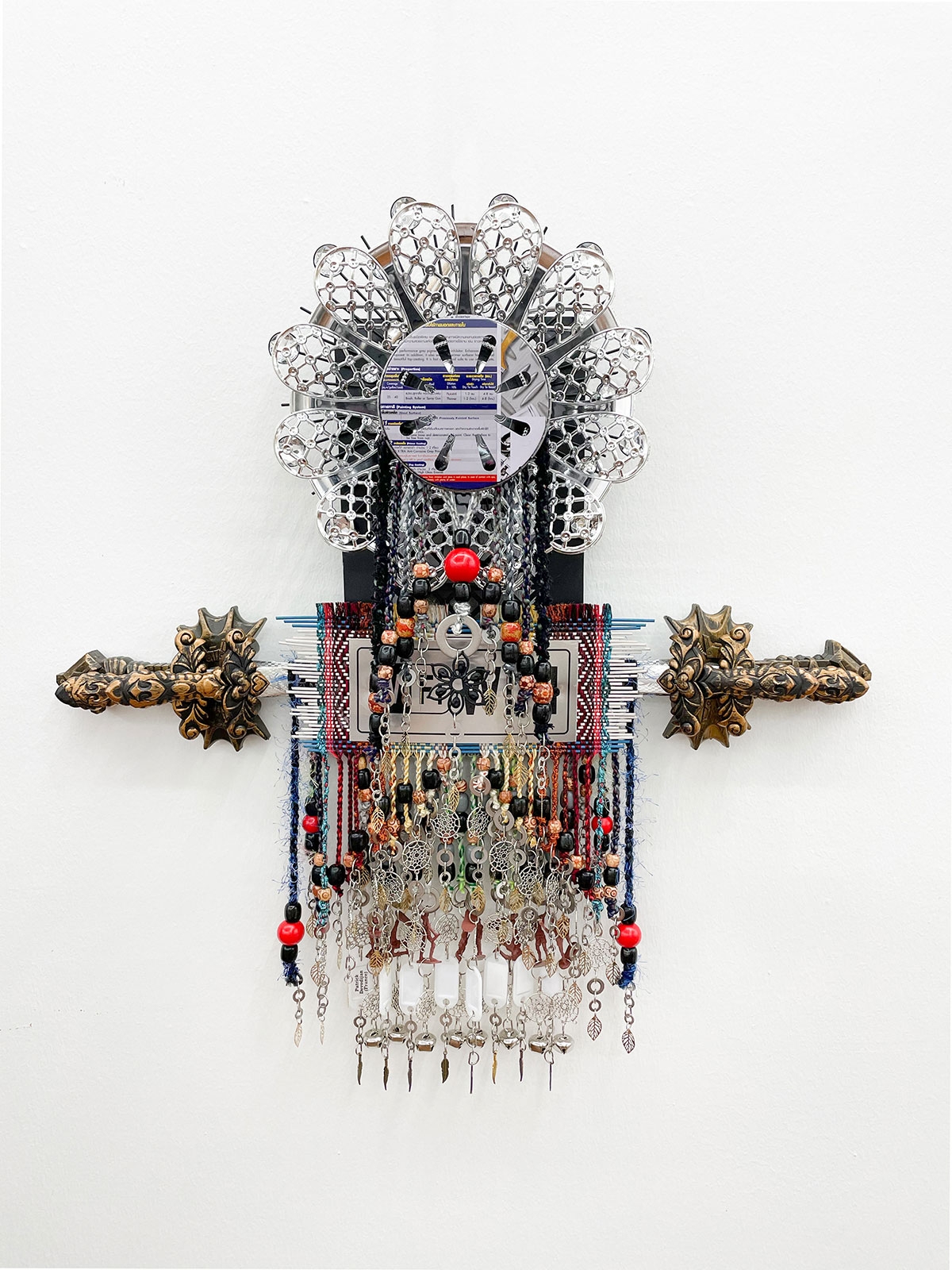 Hanging sculpture made from yarn, rakes, woven belts, beads, and metal and plastic ornaments