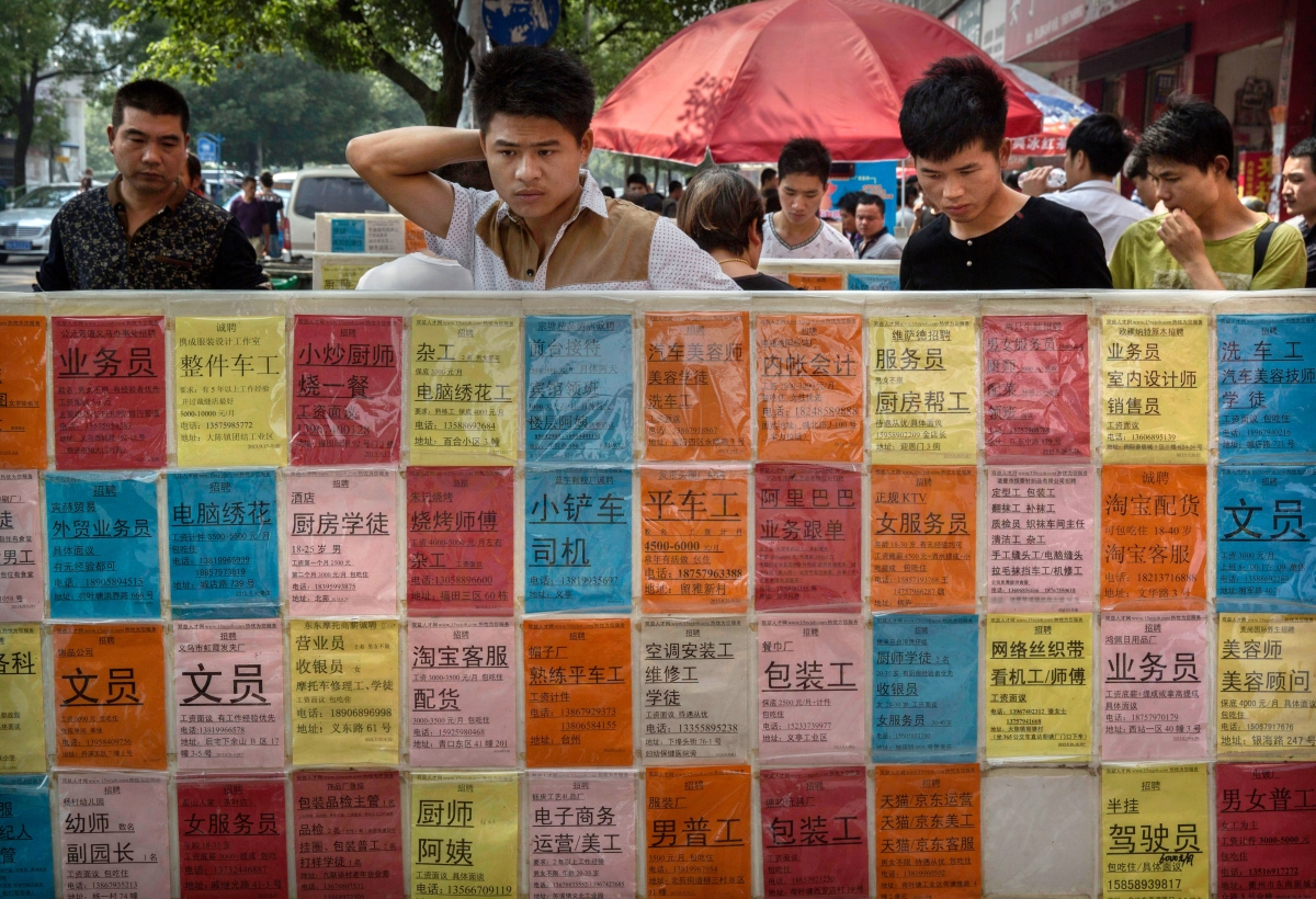 Chinese men look at bulletin boards showing potential jobs outside a job center