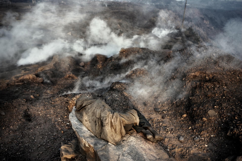 An illegal miner rests and breaths carbon monoxide coming from underground burning coal. (Erik Messori)