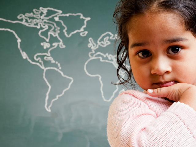 A child sits in front of a chalkboard map of the world.
