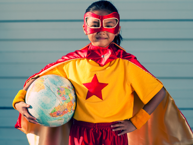 Girl dressed as superhero holding globe. (RichVintage/iStockPhotos)