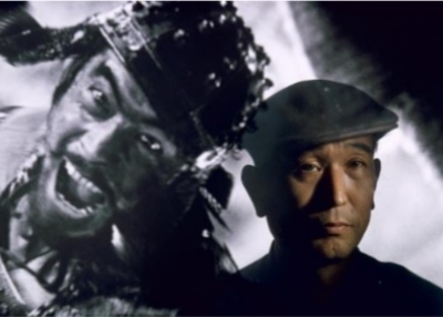 Brian Brake: Film director Akira Kurosawa standing before an image of his principal star, Toshiro Mifune, Tokyo, Japan, 1963
