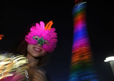 A mask seller stands outside as Caton tower illuminates during a light show rehersal for the opening ceremony for the 16th Asian Games, in Guangzhou on November 10, 2010.