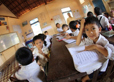 A young student looks up from his book to pose for a photo in Cambodia on May 8, 2013. (GPE/Natasha Graham/Flickr)