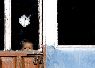A child peeks out through the glass pane of an old wooden door in Nepal on January 2, 2016. (MIRKO MARCHETTI/Flickr)