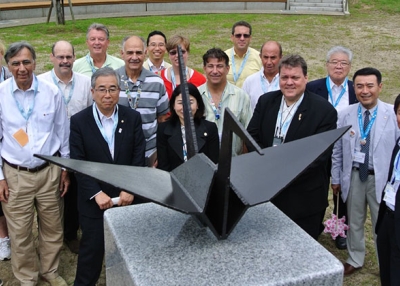 Participants in an exchange between 9/11 and 3/11 survivors pose in Kaisezan Park, Koriyama, Fukushima Prefecture with a steel origami crane in 2013. The crane was fashioned from World Trade Center wreckage and presented by the 9/11 Tribute Center on the first outreach trip in 2012. (9/11 Tribute Center)