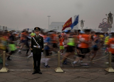Runners in masks file past a soldier during the Beijing Marathon. (Kevin Frayer/Getty Images)