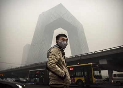 A man wears a mask as he waits to cross the road near the CCTV building in Beijing during heavy smog on November 29, 2014. (Kevin Frayer/Getty Images)
