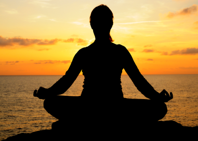A woman meditating facing the sunset